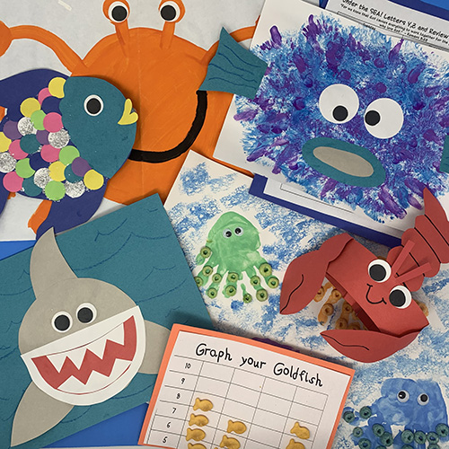 Under the sea projects compiled together showing a shark cut out, a lobster hat, a fish with many scales, and various worksheets